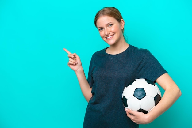 Giovane donna del giocatore di calcio isolata su sfondo blu che punta il dito verso il lato