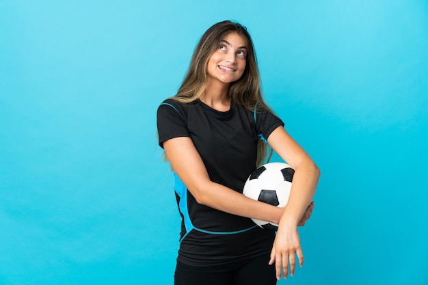 Giovane donna del giocatore di football americano isolata sulla parete blu che pensa un'idea mentre osserva in su