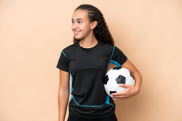 Giovane donna del giocatore di gioco del calcio isolata sul lato di sguardo del fondo beige