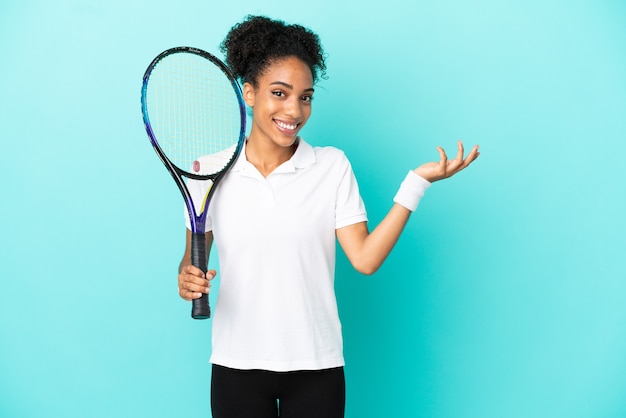 Giovane donna del giocatore di tennis isolata su fondo blu che estende le mani al lato per invitare a venire