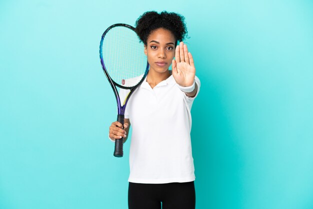 Giovane donna del giocatore di tennis isolata su fondo blu che fa gesto di arresto