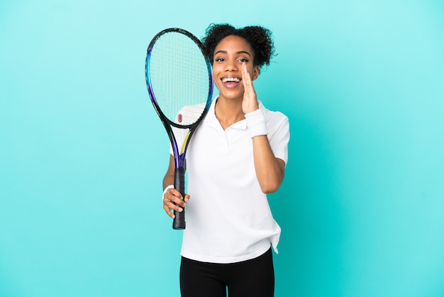 Giovane donna del giocatore di tennis isolata su fondo blu che grida con la bocca spalancata