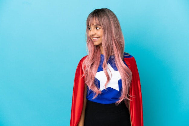 Giovane donna del supereroe con capelli rosa isolata su fondo blu che guarda al lato e che sorride