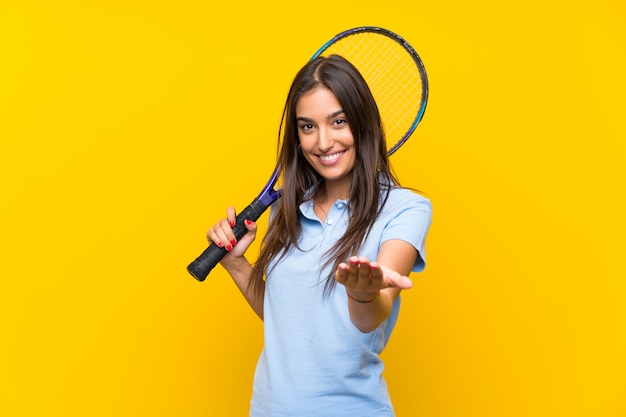 Giovane donna del tennis sopra la parete gialla isolata che invita a venire con la mano. Felice che tu sia venuto