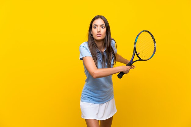 Giovane donna del tennis sopra la parete gialla isolata
