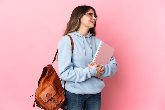 Giovane donna dell'allievo isolata sulla parete rosa che osserva lato