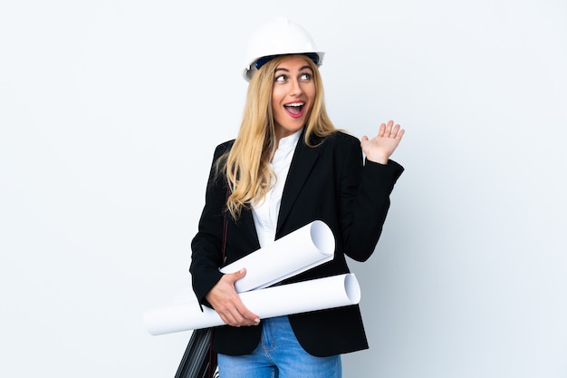 Giovane donna dell'architetto con il casco e che tiene i modelli isolati con l'espressione facciale di sorpresa