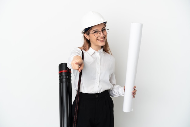 Giovane donna dell'architetto con il casco e che tiene i modelli isolati su fondo bianco che indica la parte anteriore con l'espressione felice