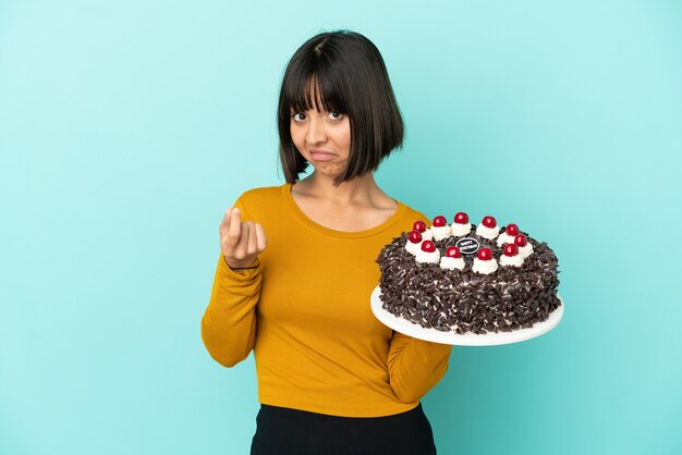 Giovane donna della corsa mista che tiene la torta di compleanno che fa il gesto dei soldi