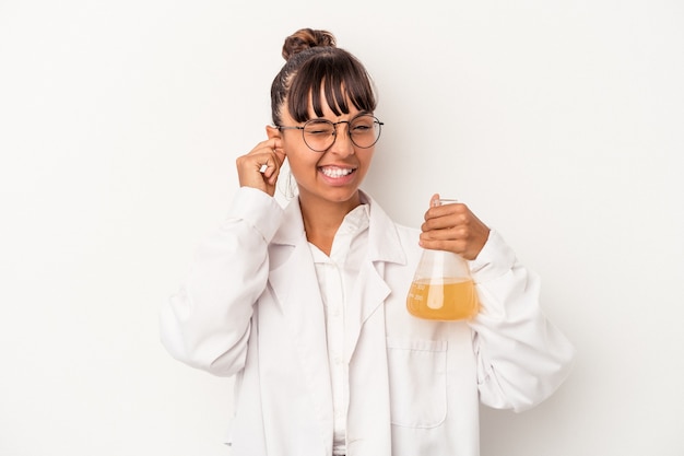 Giovane donna dello scienziato della corsa mista che tiene una provetta isolata su fondo bianco che copre le orecchie con le mani.