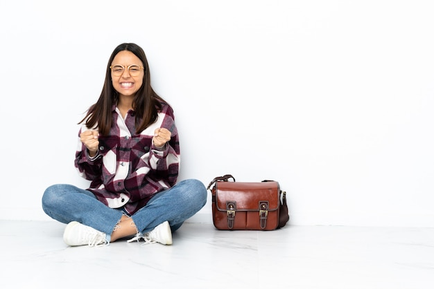 Giovane donna dello studente che si siede sul pavimento che celebra una vittoria nella posizione del vincitore