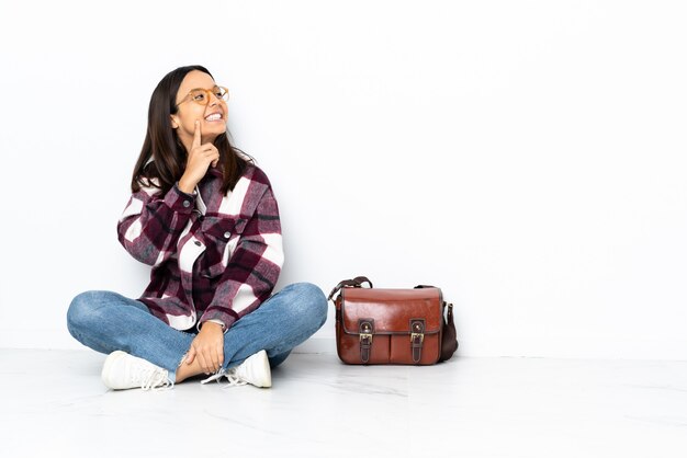 Giovane donna dello studente che si siede sul pavimento che pensa un'idea mentre guardando su