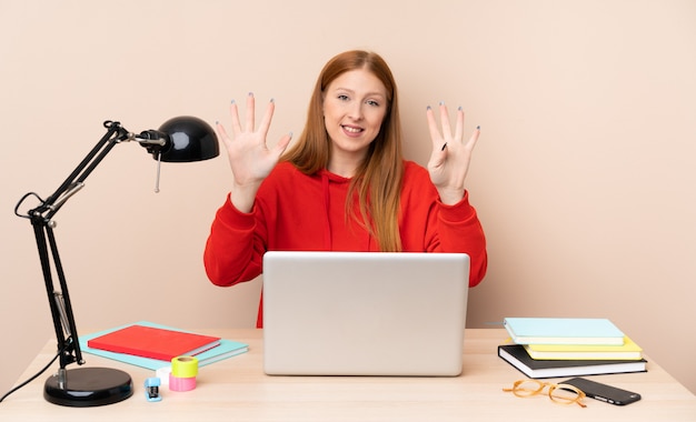 Giovane donna dello studente in un posto di lavoro con un computer portatile che conta nove con le dita