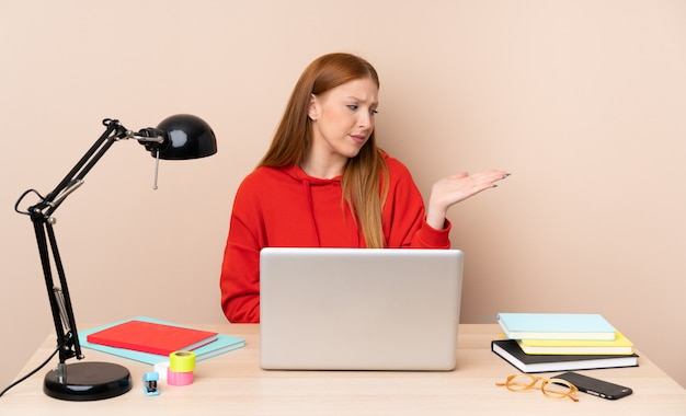 Giovane donna dello studente in un posto di lavoro con un computer portatile che tiene qualcosa