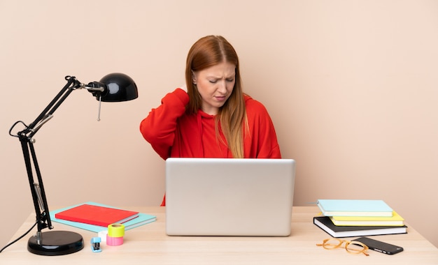 Giovane donna dello studente in un posto di lavoro con un computer portatile con il mal di collo