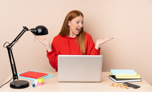 Giovane donna dello studente in un posto di lavoro con un copyspace della tenuta del computer portatile con due mani