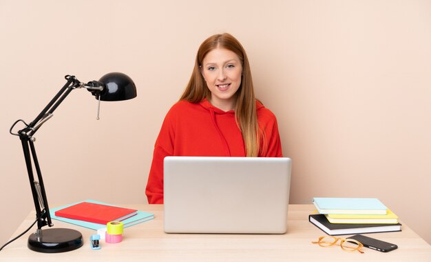 Giovane donna dello studente in un posto di lavoro con una risata del computer portatile