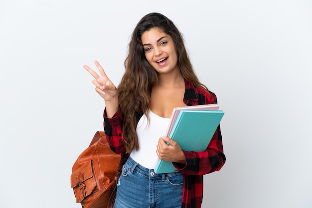 Giovane donna dello studente isolata su fondo bianco che sorride e che mostra il segno di vittoria