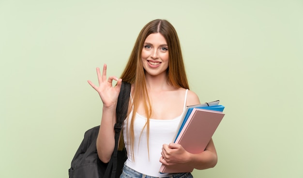 Giovane donna dello studente sopra verde isolato che mostra un segno giusto con le dita