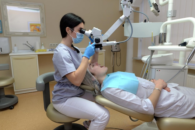 Giovane donna dentista che tratta i canali radicolari utilizzando il microscopio nella clinica dentale Uomo paziente sdraiato sulla poltrona del dentista con la bocca aperta Medicina odontoiatria e concetto di assistenza sanitaria Apparecchiature dentali