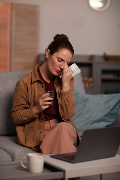 Giovane donna depressa che piange mentre era seduto sul divano e parla online sul portatile con il suo psicologo
