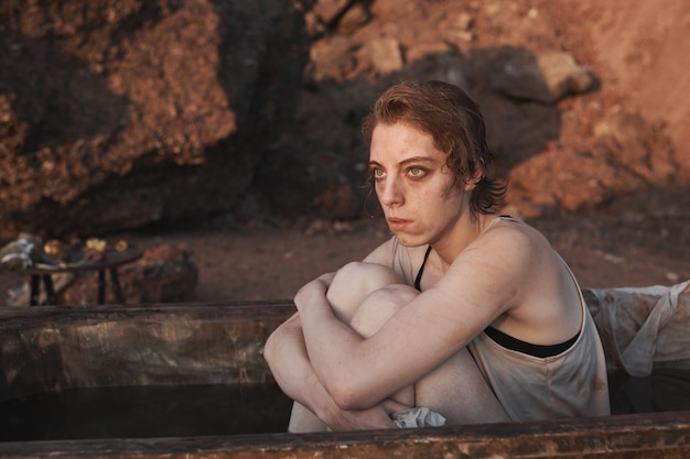 Giovane donna depressa seduta in un bagno sporco guardando il tramonto e pensando a qualcosa all'aperto