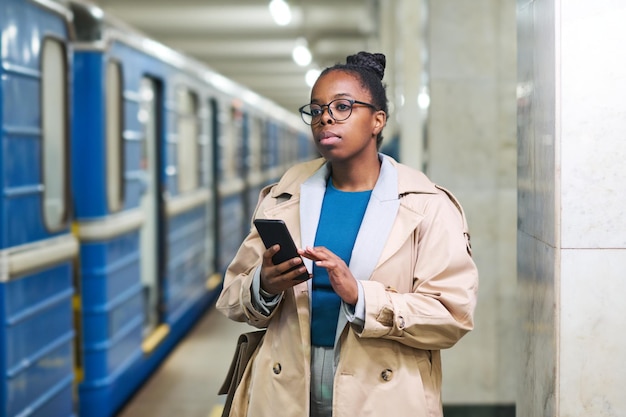 Giovane donna di affari afroamericana con il telefono cellulare in piedi nella stazione della metropolitana