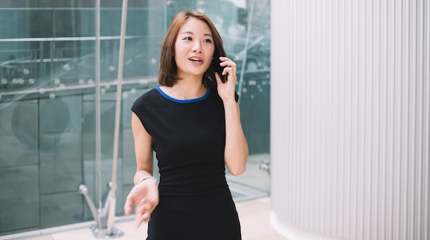 Giovane donna di affari allegra in vestito elegante che parla sul cellulare nel corridoio dell'edificio commerciale