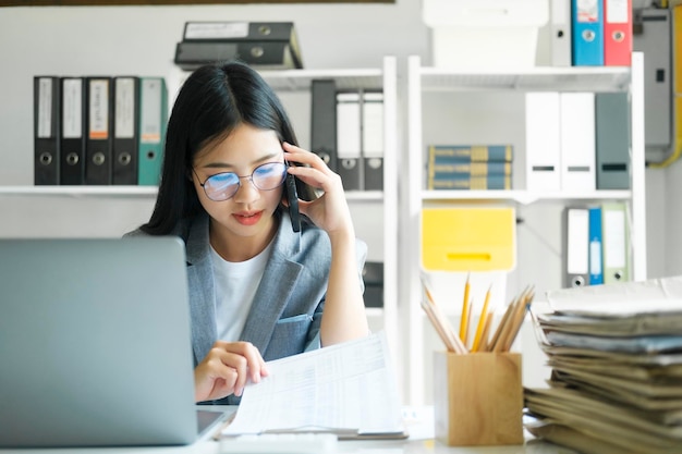 Giovane donna di affari asiatica che lavora all'ufficio facendo uso del computer portatile