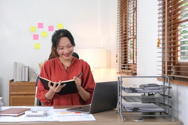 Giovane donna di affari asiatica che prende appunti usando un computer portatile nell'ufficio moderno