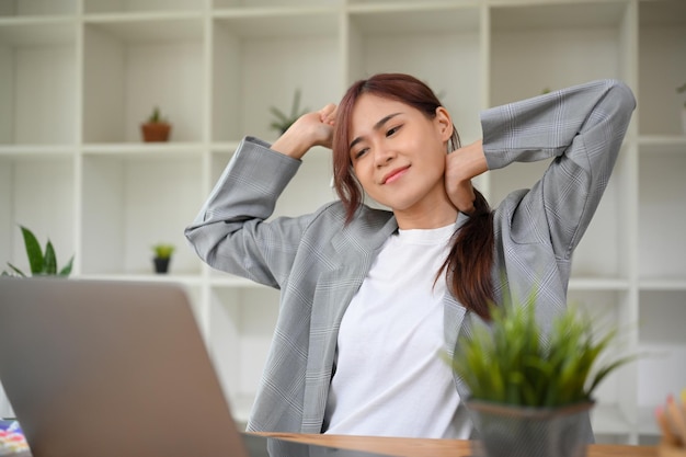 Giovane donna di affari asiatica che si rilassa e allunga le braccia e il collo dopo il lavoro
