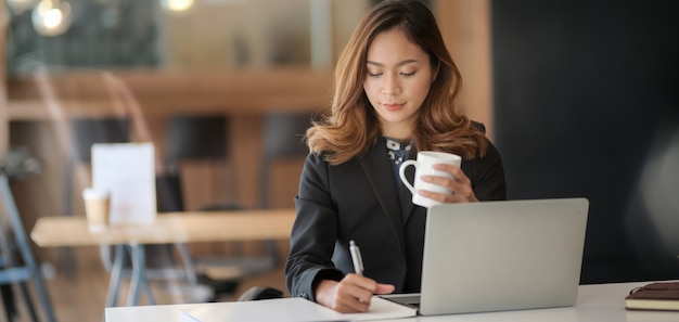 Giovane donna di affari asiatica professionale che lavora al suo progetto mentre scrivendo sul computer portatile in ufficio moderno