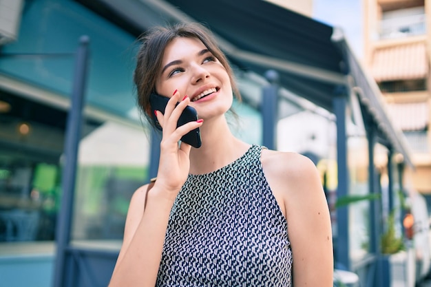 Giovane donna di affari caucasica che sorride felice parlando sullo smartphone in città.