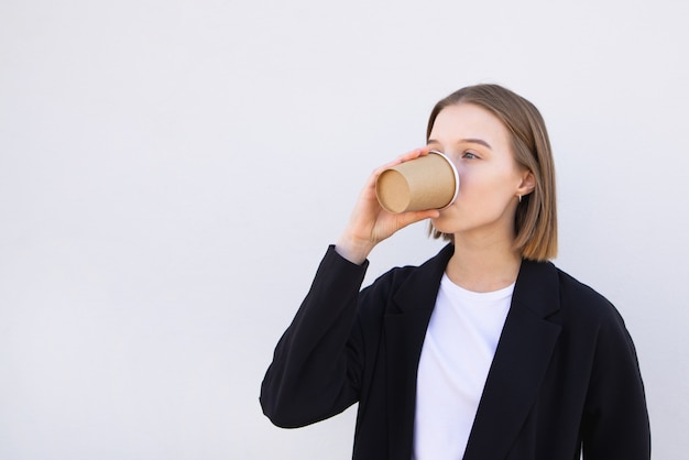 giovane donna di affari che beve caffè da una tazza di carta su bianco.