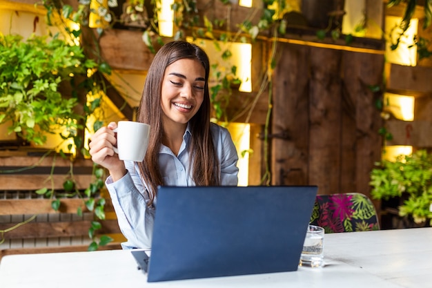 Giovane donna di affari che beve caffè e che utilizza computer portatile nella caffetteria