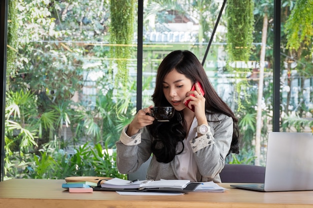 giovane donna di affari che lavora con il computer portatile mobile e che tiene tazza di caffè in ufficio