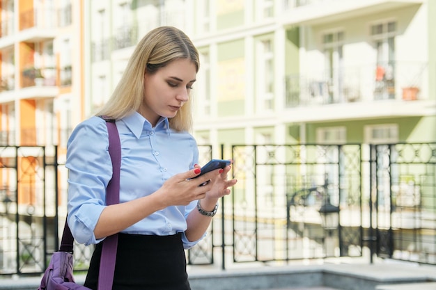 Giovane donna di affari con lo sfondo dell'edificio per uffici di strada dello smartphone