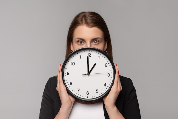 Giovane donna di affari in orologio nero della tenuta del vestito vicino al fronte isolato su gray