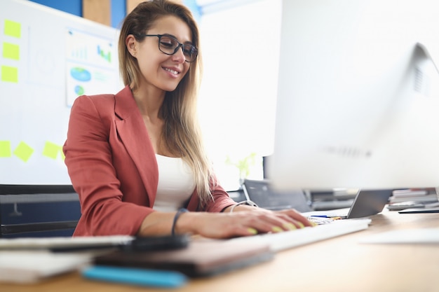 Giovane donna di bellezza che per mezzo del pc sul ritratto del posto di lavoro.