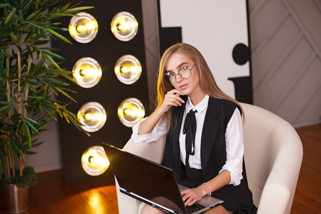 Giovane donna di bellezza in ubicazione di vetro nell'ufficio con il computer portatile.