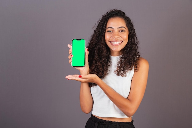 Giovane donna di colore brasiliana che tiene il cellulare e mostra la foto pubblicitaria dello schermo