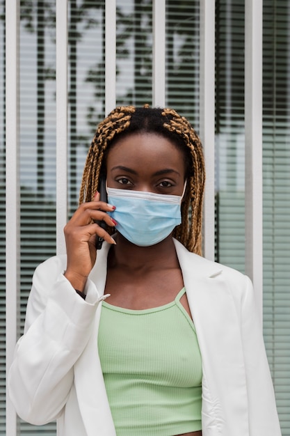 giovane donna di colore che guarda l'obbiettivo con il cellulare e la maschera per il viso Immagine verticale Copia spazio