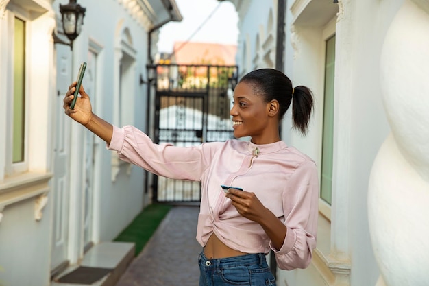 Giovane donna di colore che prende il selfie del telefono e che tiene la carta di credito