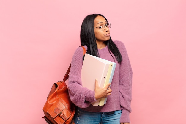 Giovane donna di colore che scrolla le spalle, sentendosi confusa e incerta, dubbiosa con le braccia incrociate e lo sguardo perplesso. concetto di studente