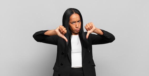 giovane donna di colore che sembra triste, delusa o arrabbiata, mostrando il pollice verso il basso in disaccordo, sentendosi frustrata. concetto di business