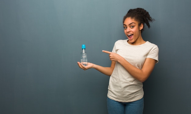 Giovane donna di colore che tiene qualcosa con la mano. Lei è in possesso di una bottiglia d&#39;acqua.