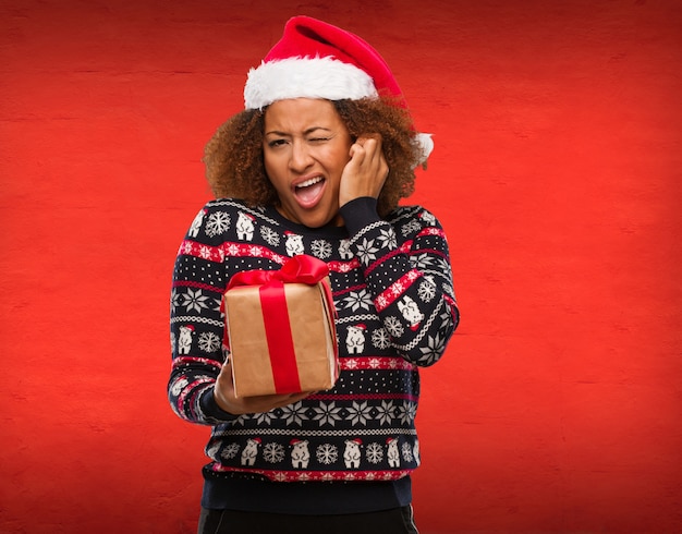 Giovane donna di colore che tiene un regalo in orecchie di copertura di giorno di Natale con le mani