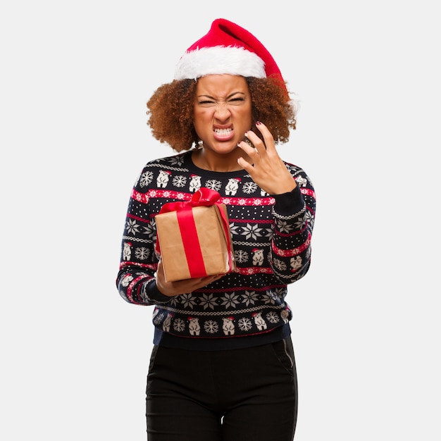 Giovane donna di colore che tiene un regalo nel giorno di Natale arrabbiato e turbato