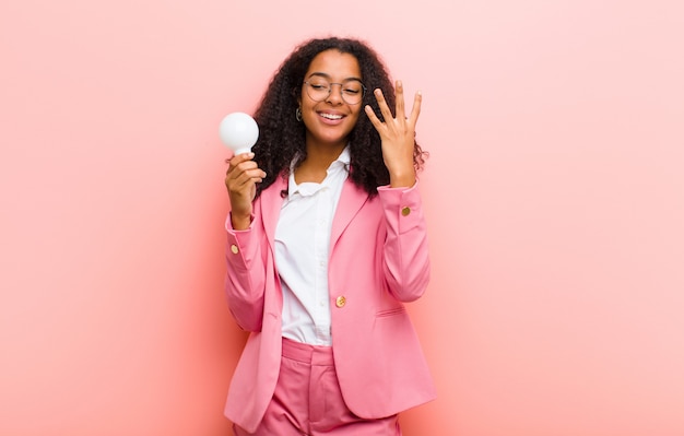Giovane donna di colore con una lampadina che ha un'idea sulla parete rosa