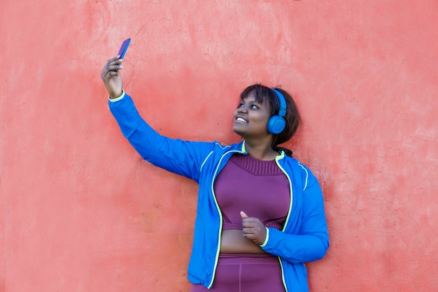 Giovane donna di colore contro un muro colorato che guarda il suo telefono cellulare facendo un selfie